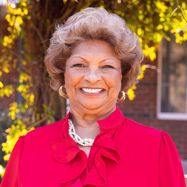 21_Healing-Transitions_EOY_Stories_Square_Maria-Spaulding_01 Maria Spaulding standing outside in red blouse smiling